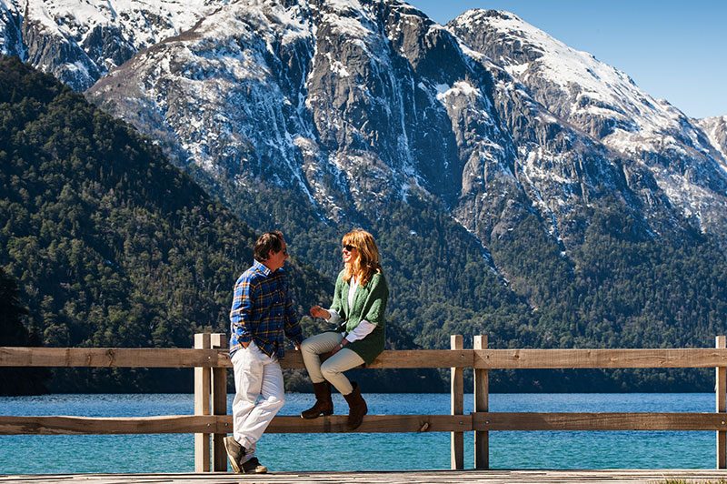 Pareja conversando junto a un lago frente a montañas nevadas en Bariloche