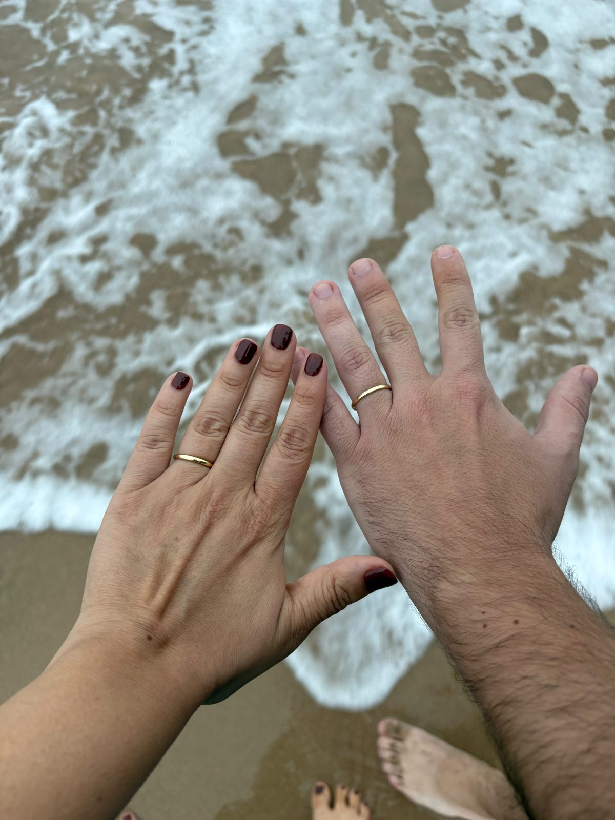 Manos de una pareja con alianzas sobre la arena y el mar en Porto de Galinhas